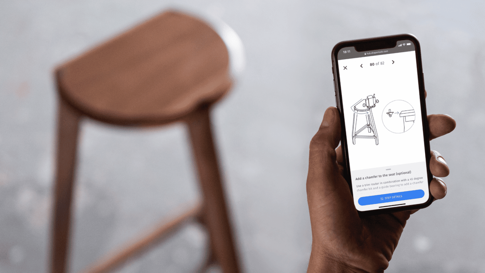 Une personne tient un smartphone affichant des instructions d'assemblage de tabouret étape par étape avec des diagrammes, tandis qu'un tabouret en bois est positionné dans l'arrière-plan flou.