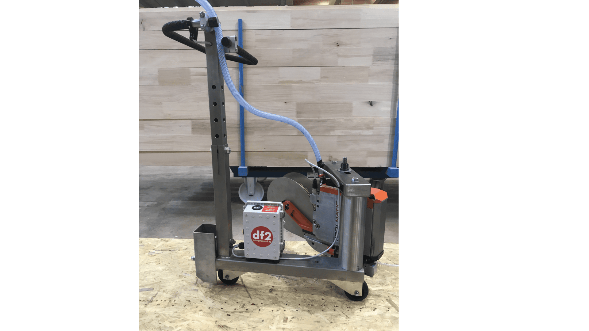 Ein Metallschneidewerkzeug mit einem langen Griff, einem Steuerkasten mit der Aufschrift df2, einem Kreismesser, Schläuchen und Rädern, das auf einer Sperrholzfläche in einer Innenwerkstatt steht. Im Hintergrund sind helle Holzplatten zu sehen.
