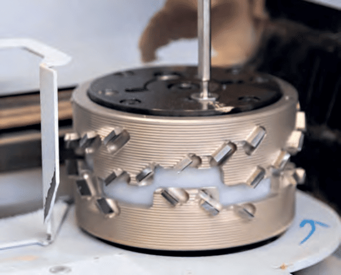 Nahaufnahme eines zylindrischen industriellen Maschinenteils mit ineinander greifenden Metallteilen und Nuten, das vertikal mit einer zentralen Stange montiert ist und wahrscheinlich für die mechanische Bearbeitung oder Fertigung verwendet wird.