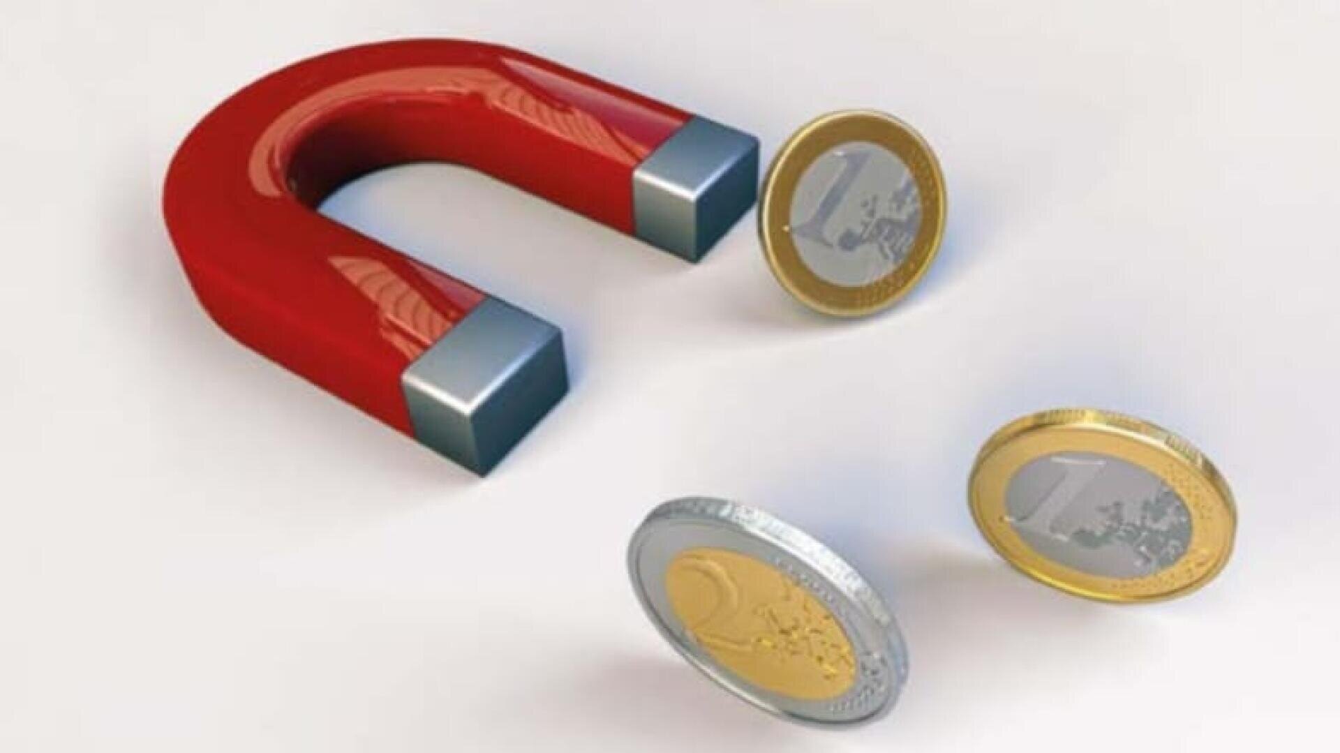Un aimant en forme de fer à cheval rouge attire trois pièces d'un euro, chacune avec une tranche métallique et un centre doré, sur un fond blanc uni.