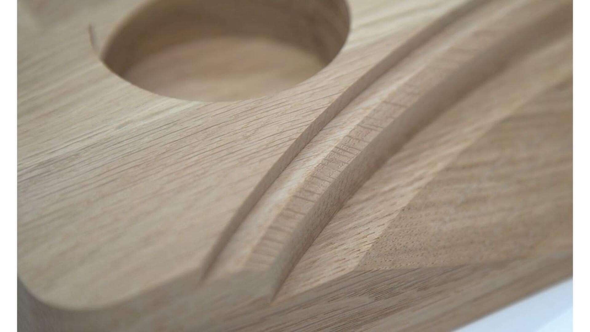 Gros plan d'une surface en bois lisse présentant un trou rond et des rainures incurvées et sculptées, mettant en valeur les détails de l'artisanat et les motifs naturels du grain du bois.