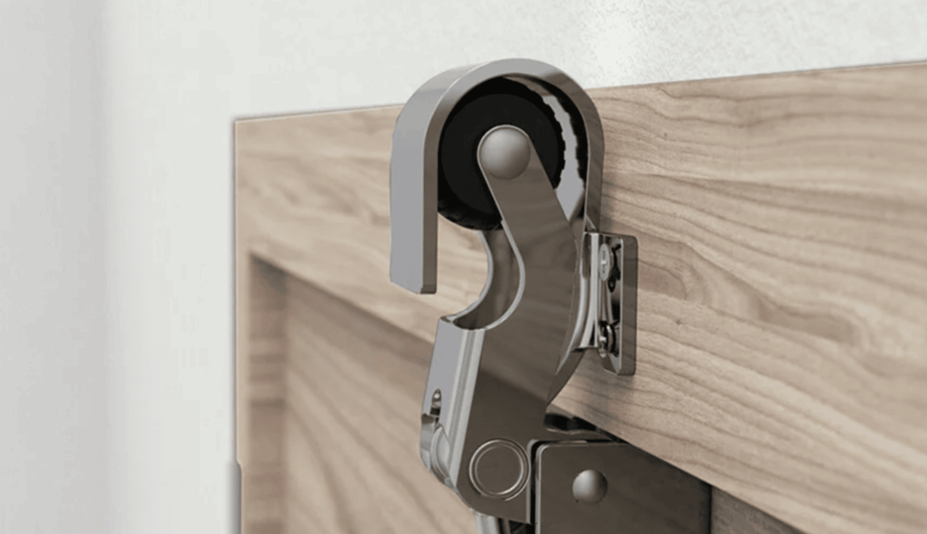 Gros plan d'une charnière de porte en métal avec un galet noir fixé au bord supérieur d'une porte en bois, montée près d'un mur blanc.