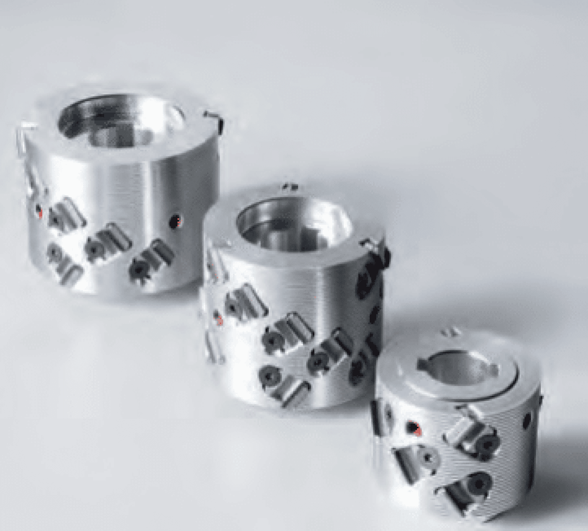 Drei zylindrische Metallschneidewerkzeuge mit mehreren eingesetzten Klingen sind auf einer hellen Fläche angeordnet; jedes Werkzeug hat eine andere Größe, und sie haben eine glänzende, bearbeitete Oberfläche mit sichtbaren Schrauben und Schlitzen.