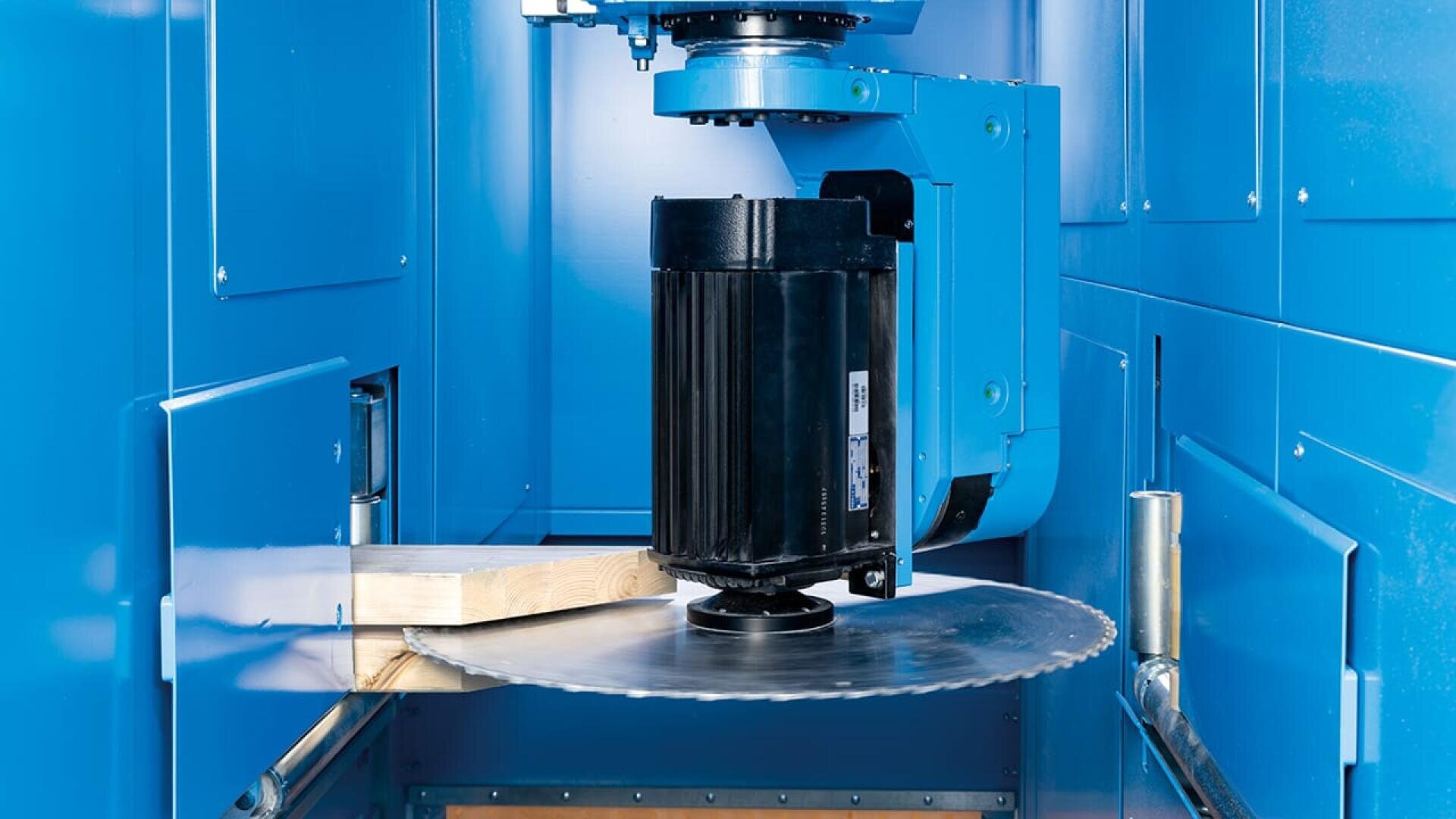 Nahaufnahme einer industriellen Sägemaschine, die ein Holzbrett in einem blauen, geschlossenen Arbeitsbereich schneidet. Das Kreissägeblatt und der Motor sind zu sehen, während das Holz zum Schneiden positioniert ist.
