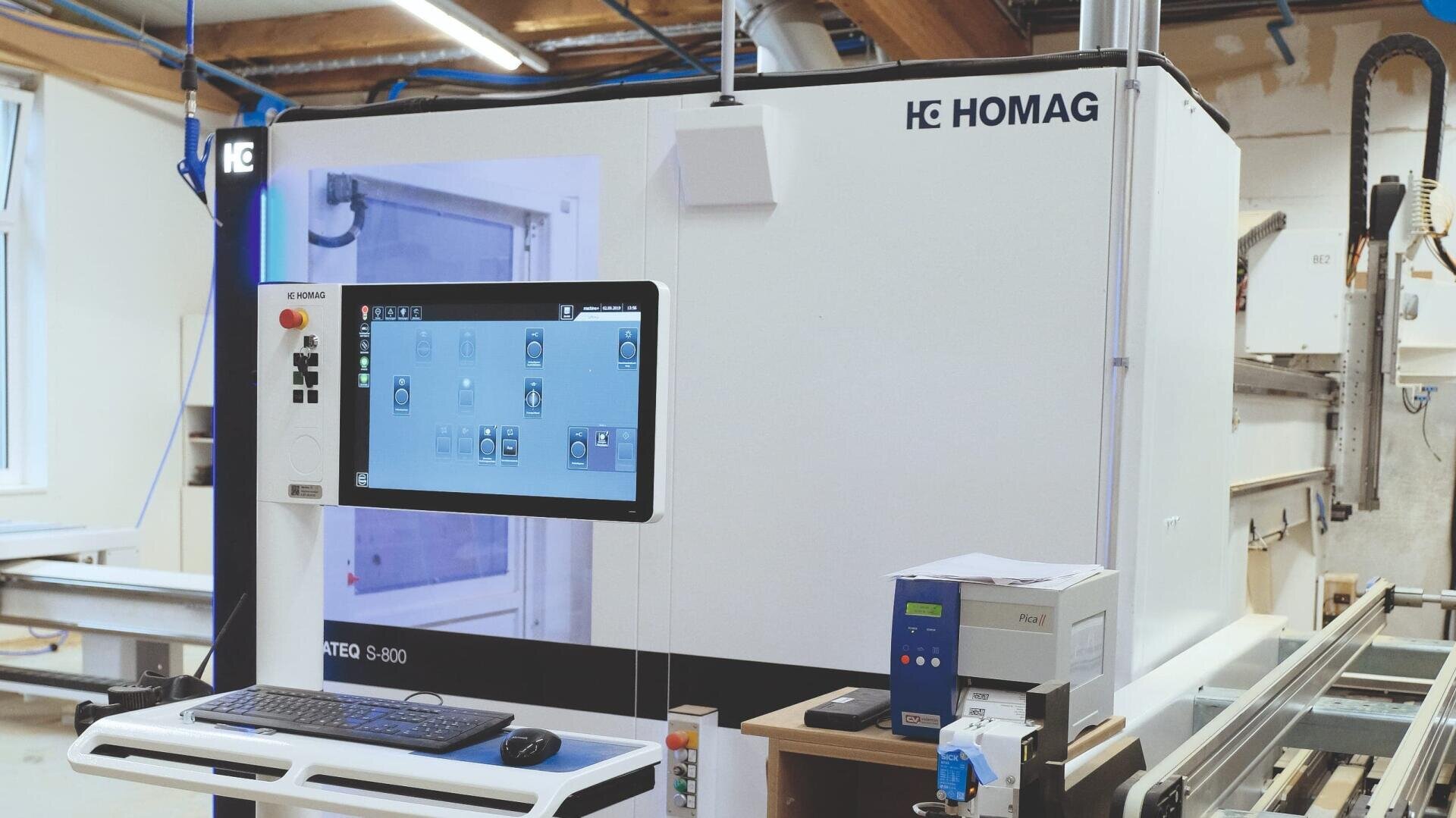 Eine automatisierte Holzbearbeitungsmaschine S-800 von HOMAG mit einem digitalen Touchscreen-Bedienfeld in einer modernen Werkstatt. Rund um die Maschine sind verschiedene Tasten und Geräte zu sehen.