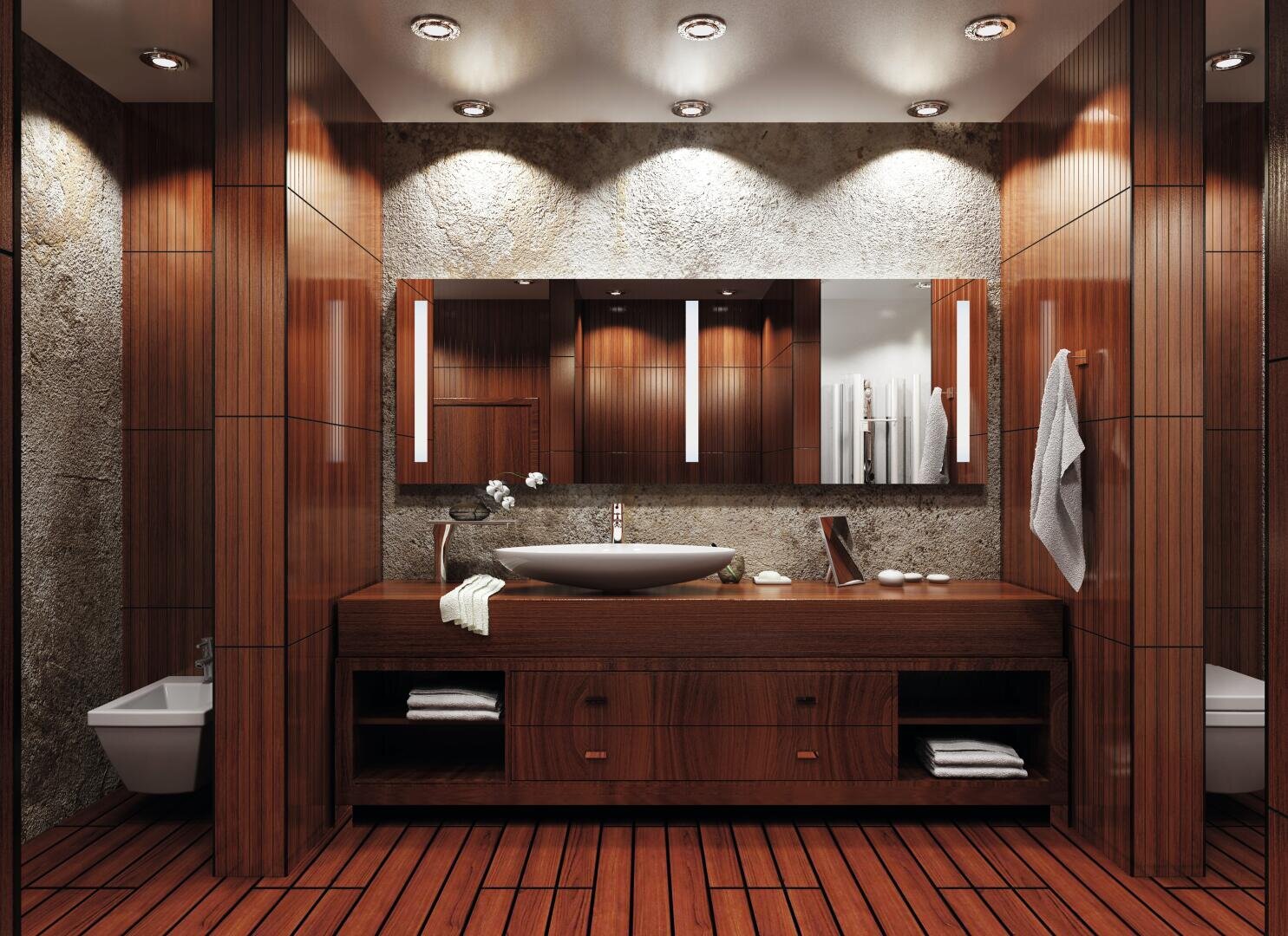 Modernes Badezimmer mit Holzwänden und -böden, einem breiten Spiegel über einem hölzernen Waschtisch mit Gefäßwaschbecken, Handtuch an der rechten Wand und eingebauter Beleuchtung an der Decke, die eine warme, elegante Atmosphäre schafft.