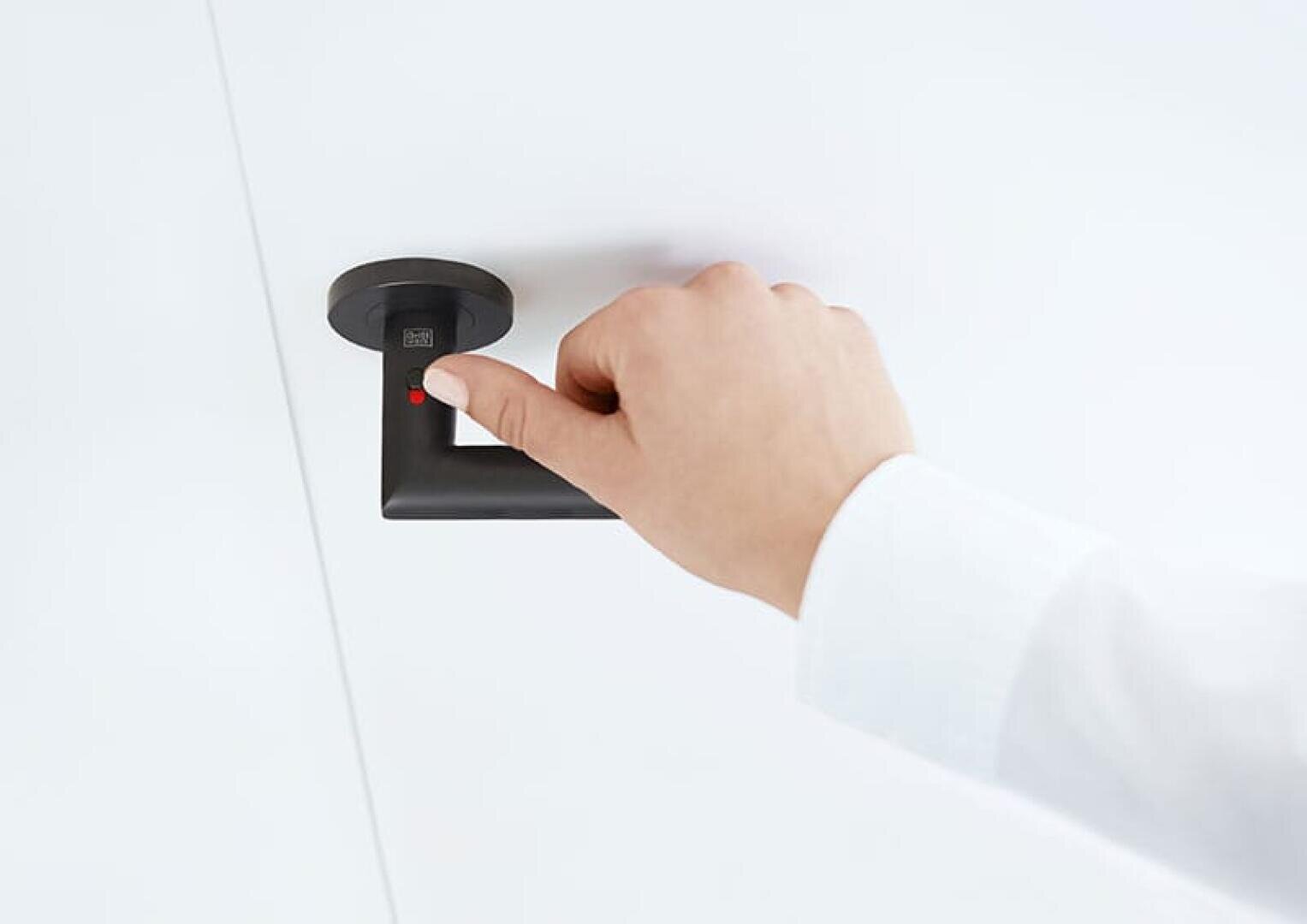 Die Hand einer Person drückt ihren Daumen auf einen Fingerabdruckscanner, der sich auf einem schwarzen Türgriff vor einem weißen Hintergrund befindet.