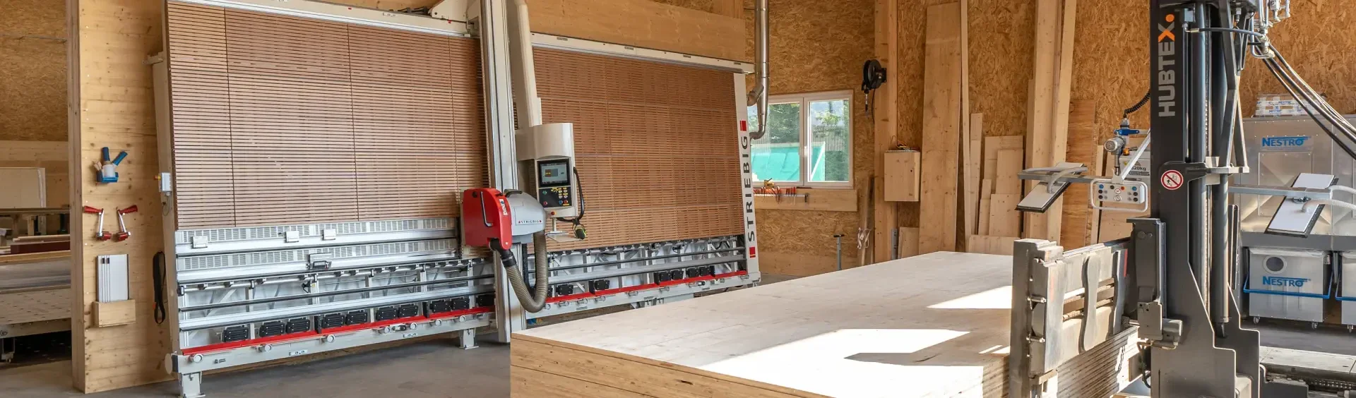 Eine Holzwerkstatt mit großen vertikalen Plattensägen, holzgetäfelten Wänden, gestapelten Hölzern und einem Gabelstapler im Vordergrund. Durch ein Fenster strömt Sonnenlicht herein und beleuchtet den organisierten Arbeitsbereich.