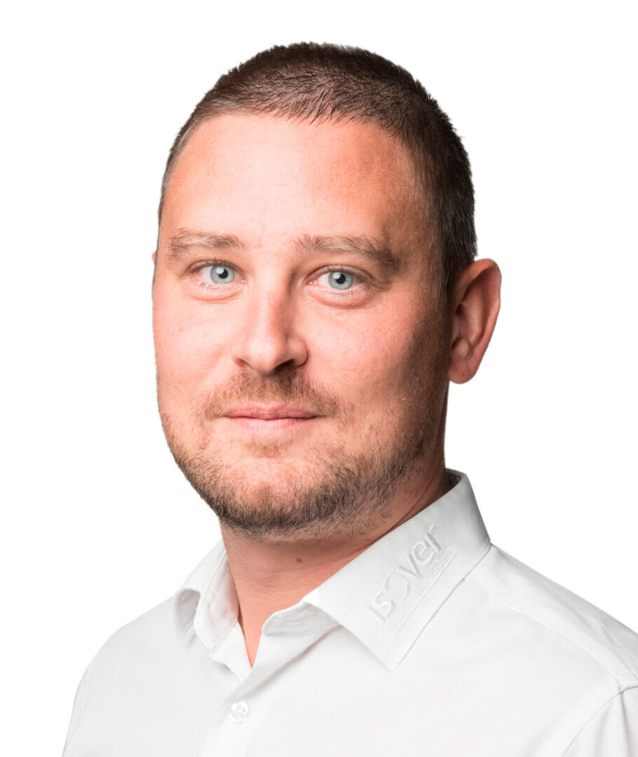 Ein Mann mit kurzen braunen Haaren und hellblauen Augen trägt ein weißes Hemd mit Kragen, auf dem Solver aufgestickt ist, und posiert vor einem schlichten weißen Hintergrund.