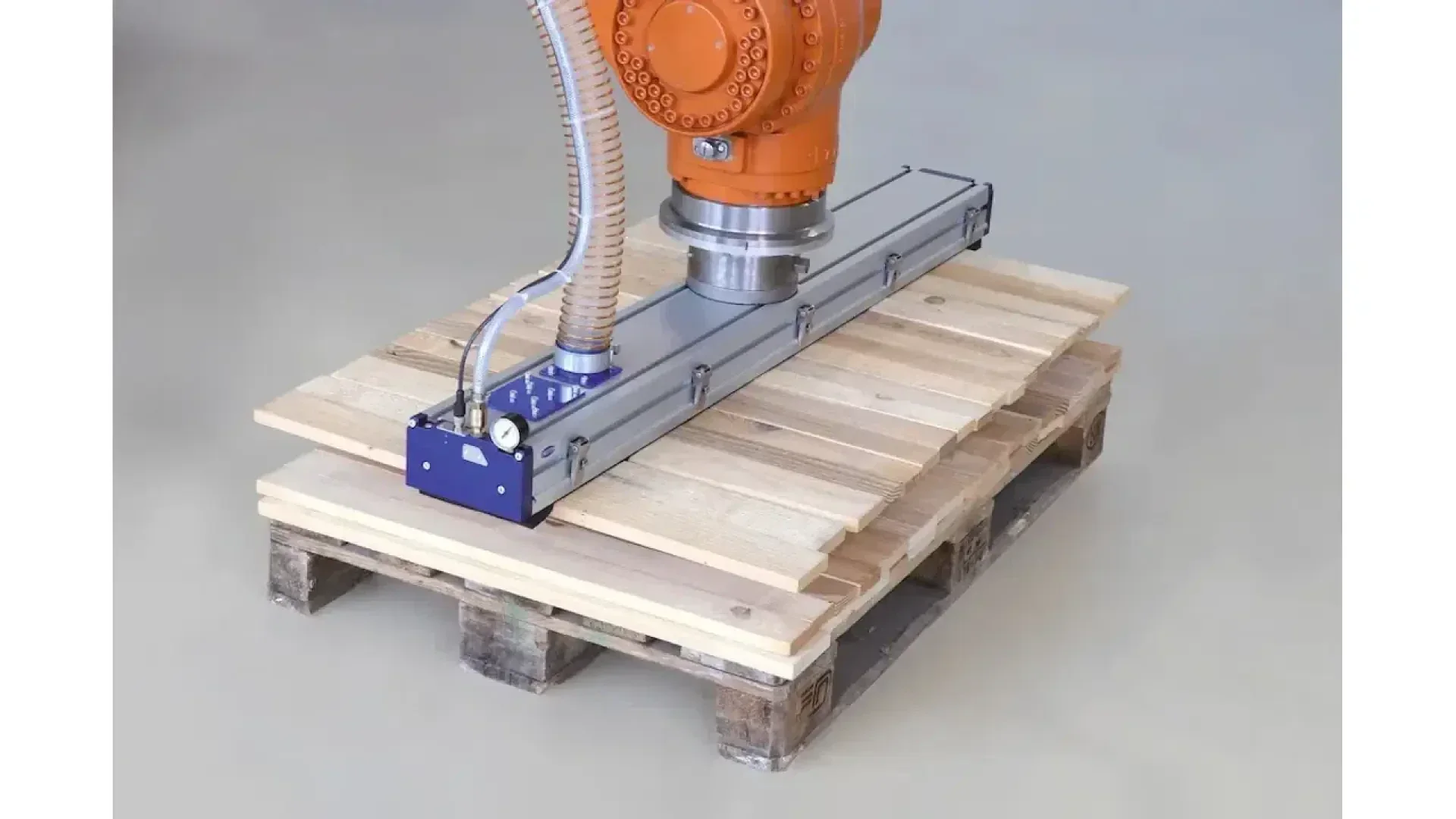 Un bras robotisé industriel équipé d'une pince à vide soulève des planches de bois empilées sur une palette en bois, faisant ainsi la démonstration d'une manutention automatisée.