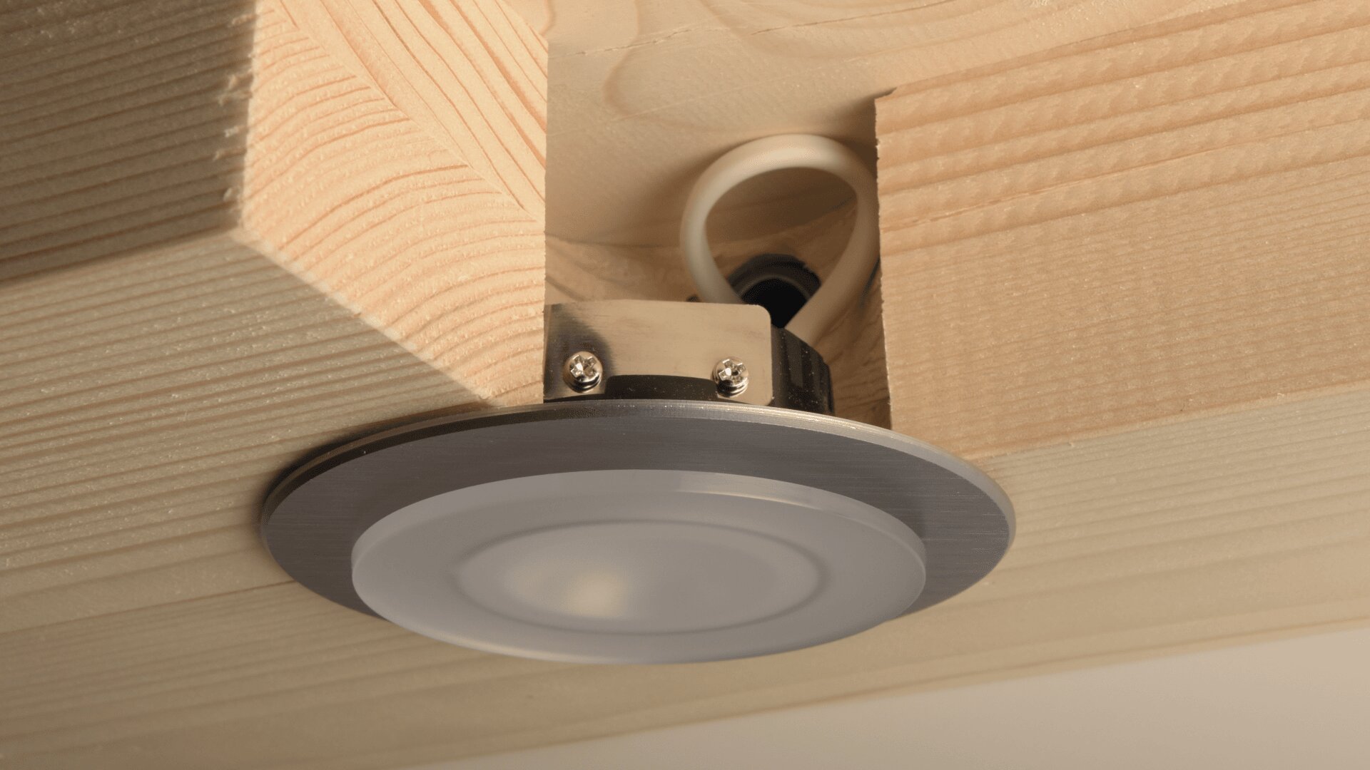 Un plafonnier LED encastré est installé dans un plafond en bois, avec un câblage visible et un support de montage fixé au bois.