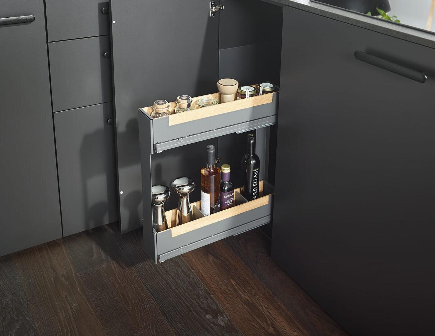 Eine moderne Küche verfügt über eine ausziehbare Schublade mit zwei Fächern, in der Gewürzdosen, Ölflaschen und Gewürze aufbewahrt werden können, eingebaut in einen schlichten dunklen Schrank über einem Holzboden.