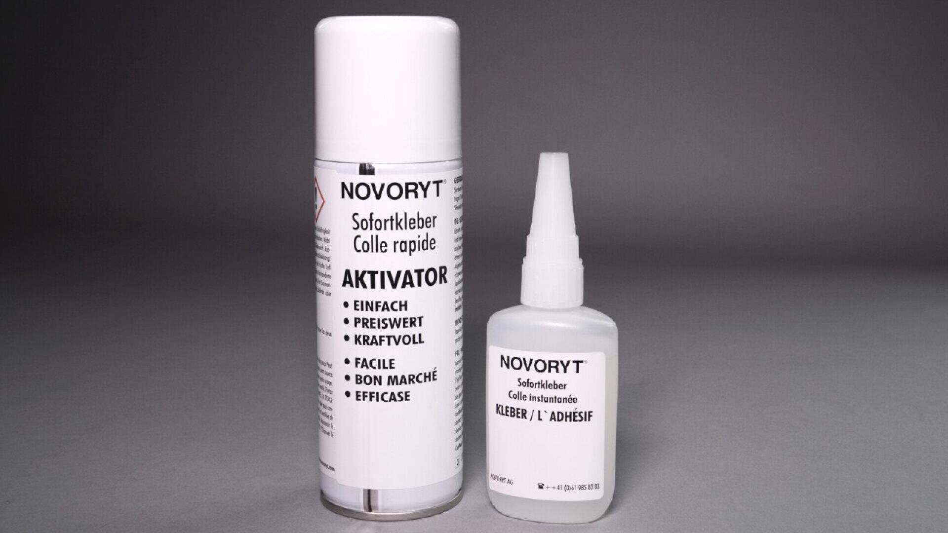Deux produits adhésifs Novoryt sur une surface grise : un grand aérosol blanc étiqueté Aktivator et un plus petit flacon de colle blanche étiqueté Sofortkleber. Les deux étiquettes comportent un texte en plusieurs langues.