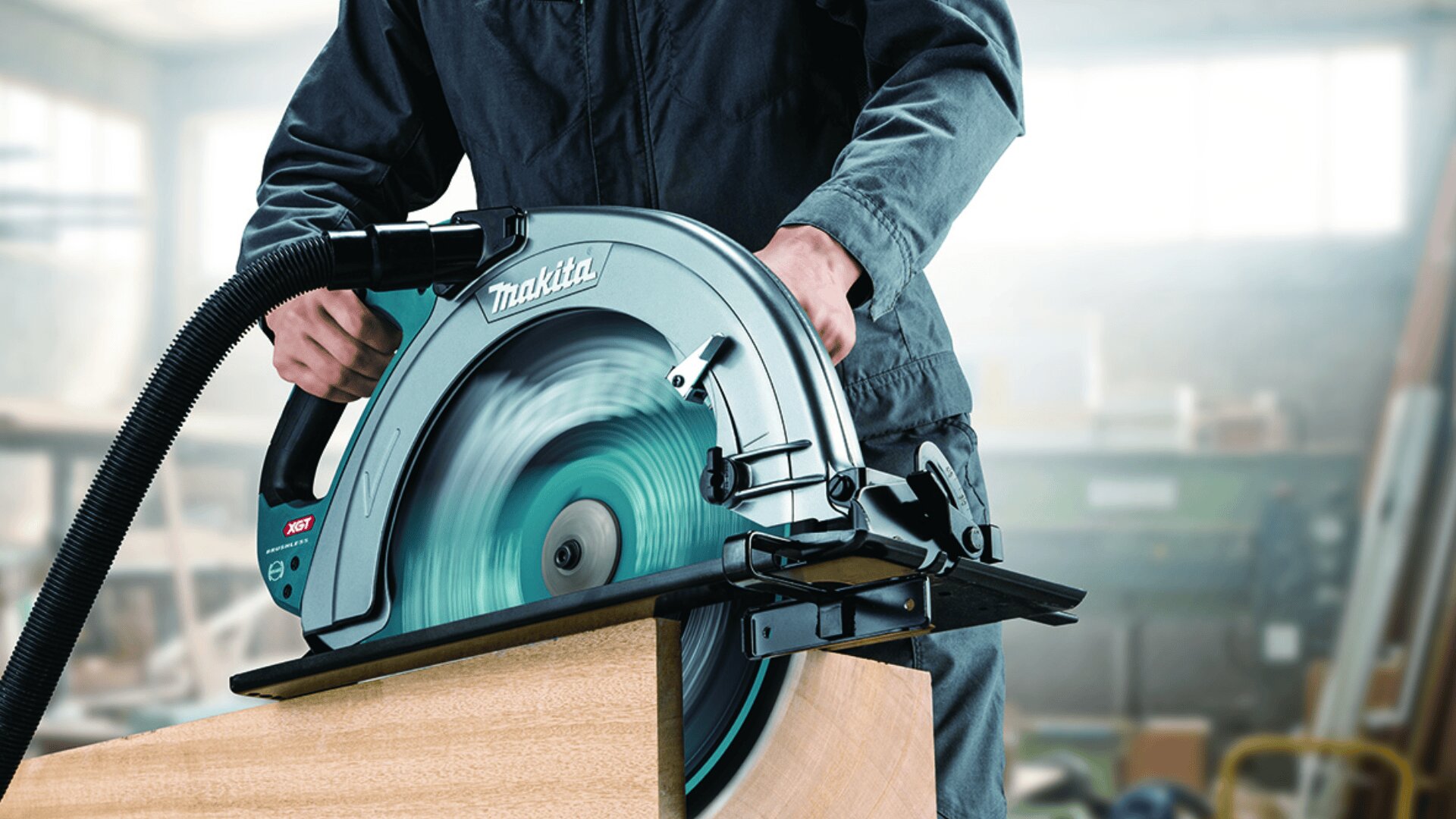 Une personne en tenue de travail utilise une scie circulaire Makita pour couper une pièce de bois dans un atelier, la sciure étant récupérée par un tuyau d'aspiration.