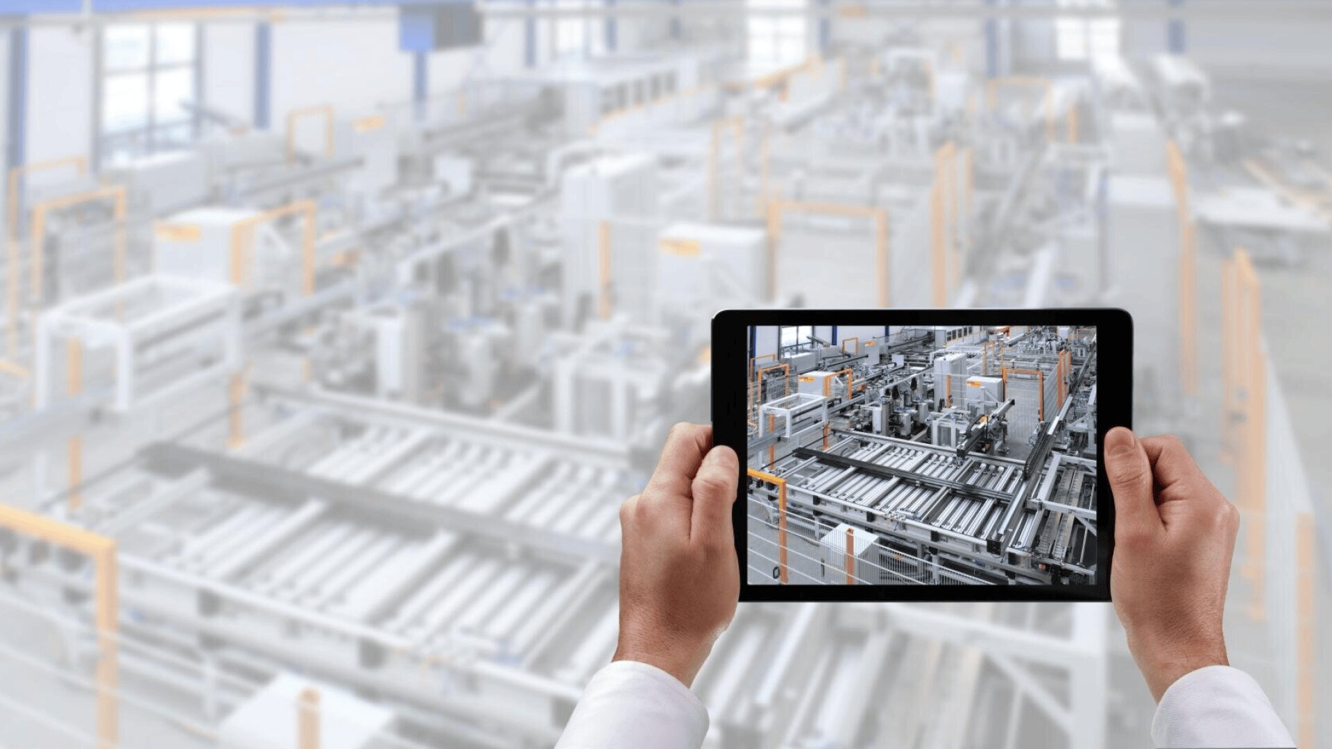 Eine Person hält ein Tablet in der Hand, auf dem ein klares Bild einer modernen Fabrik oder Fertigungsstraße zu sehen ist, das mit der gleichen unscharfen Fabrikszene im Hintergrund übereinstimmt.