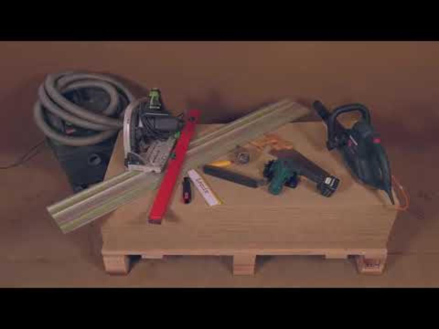 Eine Holzpalette enthält verschiedene Werkzeuge, darunter eine Kreissäge, einen elektrischen Hobel, eine rote Wasserwaage, ein Klapplineal, ein Maßband, einen Bleistift, eine Zange und einen aufgerollten Staubsaugerschlauch, alles auf einem braunen Hintergrund.