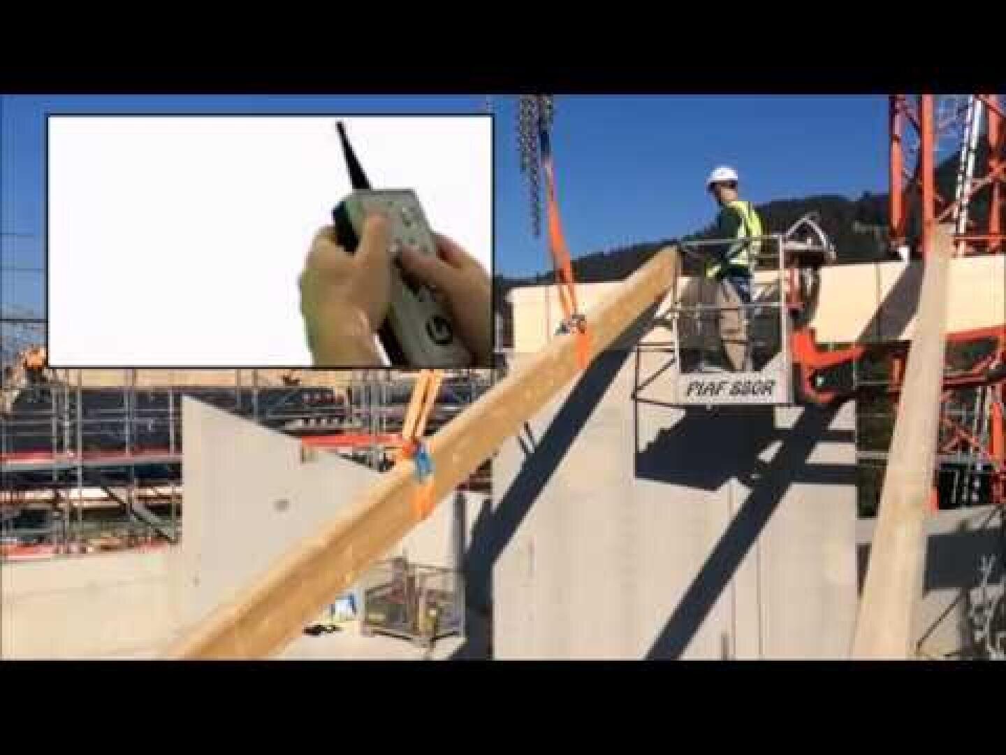 Un ouvrier de la construction portant un casque et un gilet de sécurité fait fonctionner un équipement sur un chantier. Un médaillon montre les mains qui utilisent un dispositif de commande à distance. Des échafaudages et des murs en béton sont visibles à l'arrière-plan.