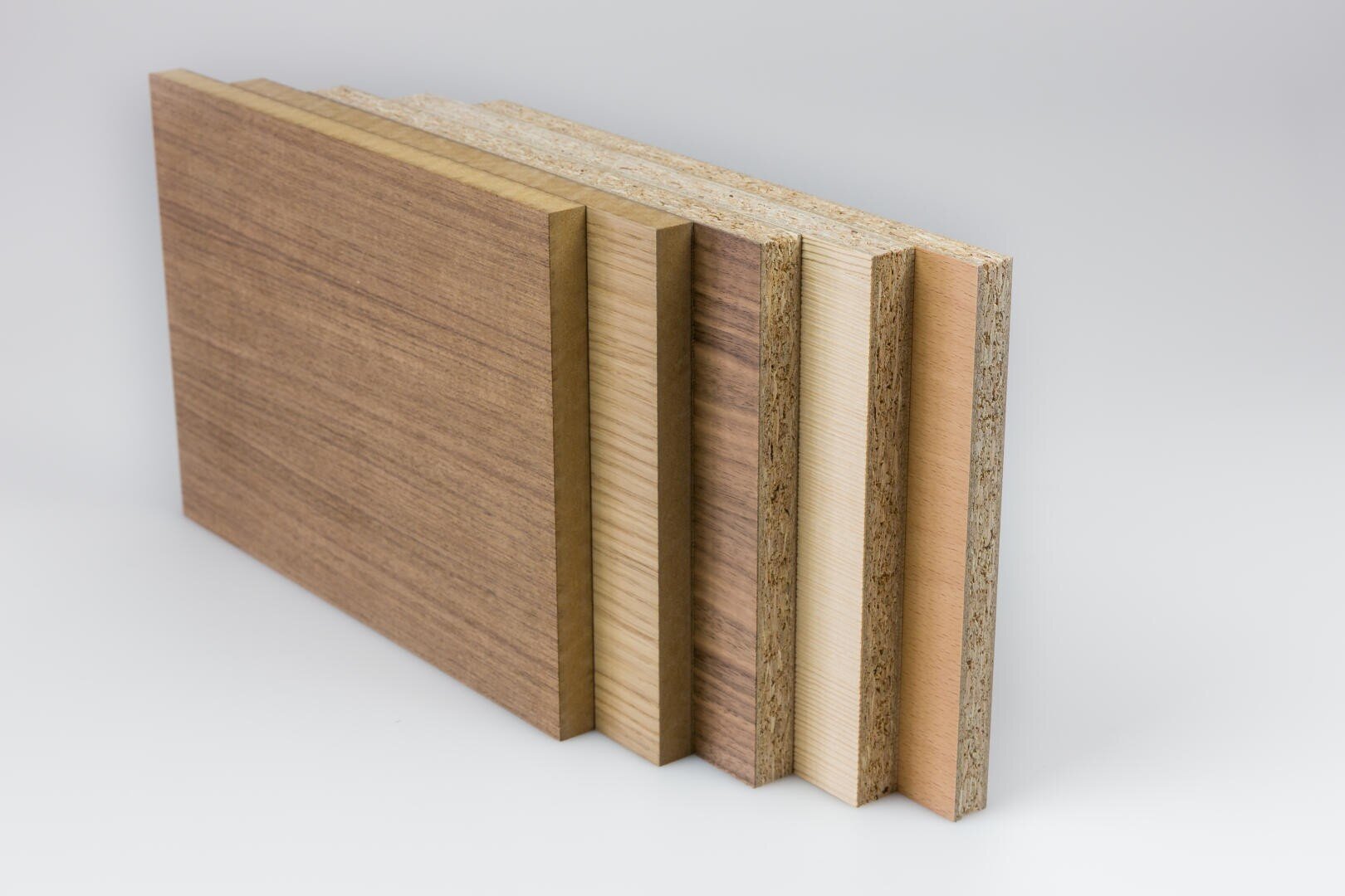 Fünf rechteckige Holzplatten von unterschiedlicher Dicke und Farbe stehen aufrecht in einer Reihe auf weißem Hintergrund und zeigen ihre geschichteten Kanten und unterschiedlichen Oberflächenstrukturen.