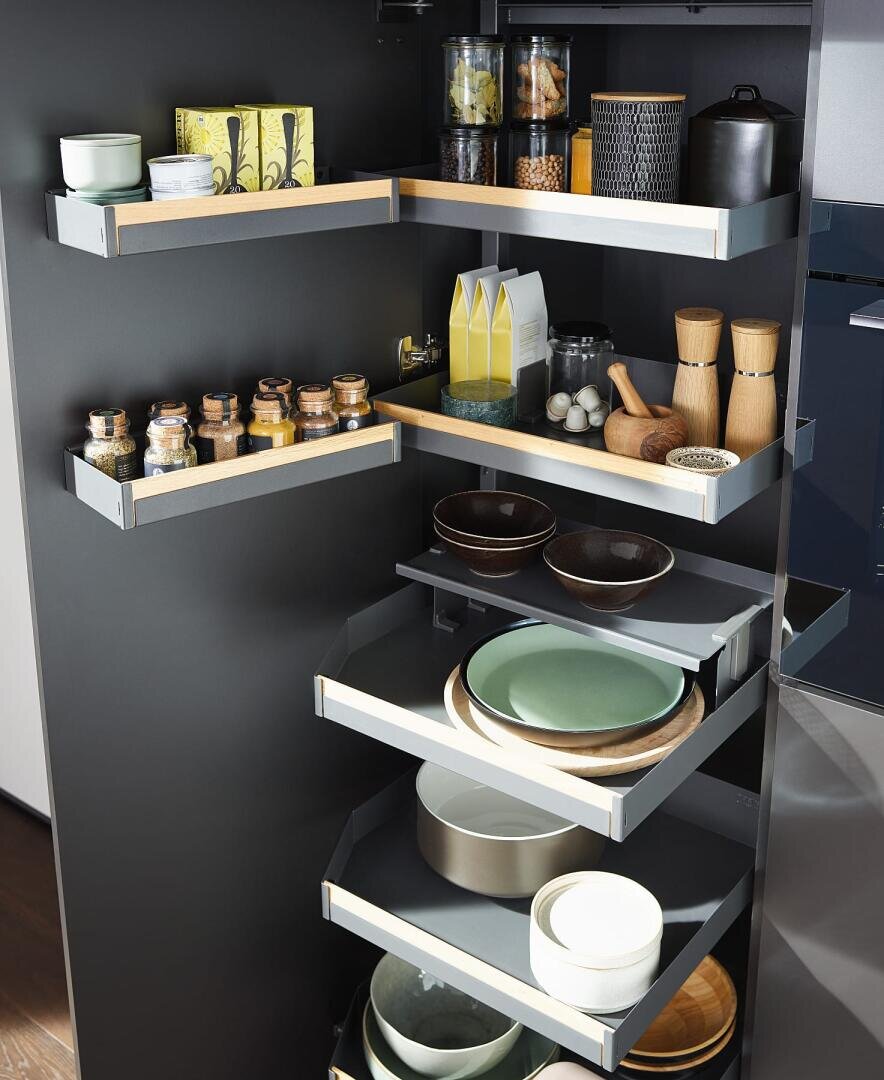 Ein moderner schwarzer Küchenschrank mit ausziehbaren Regalen, die ordentlich mit Gläsern, Gewürzen, Schüsseln, Tellern, Flaschen und Küchenutensilien bestückt sind. Die Regale sind gestaffelt und teilweise ausgezogen.