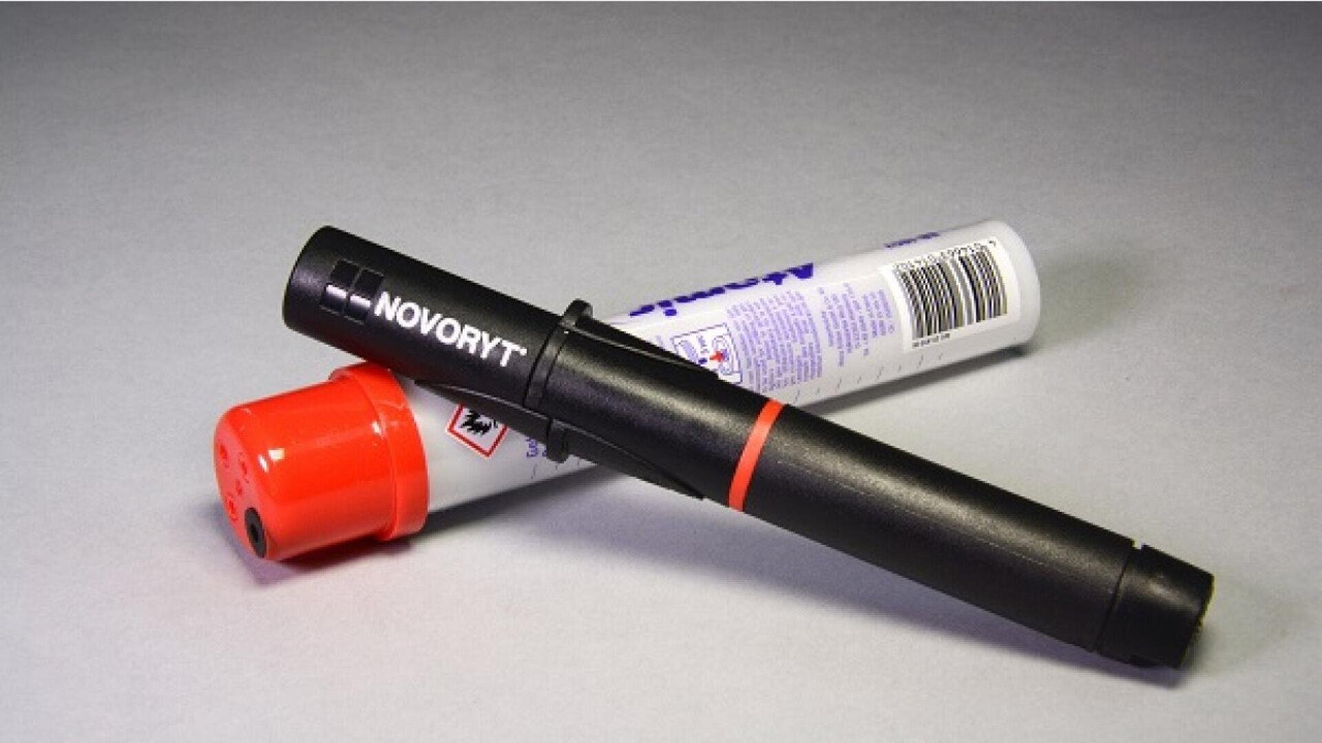 Un stylo marqueur NOVORYT noir avec un anneau rouge est placé sur un marqueur blanc et rouge posé sur une surface grise.