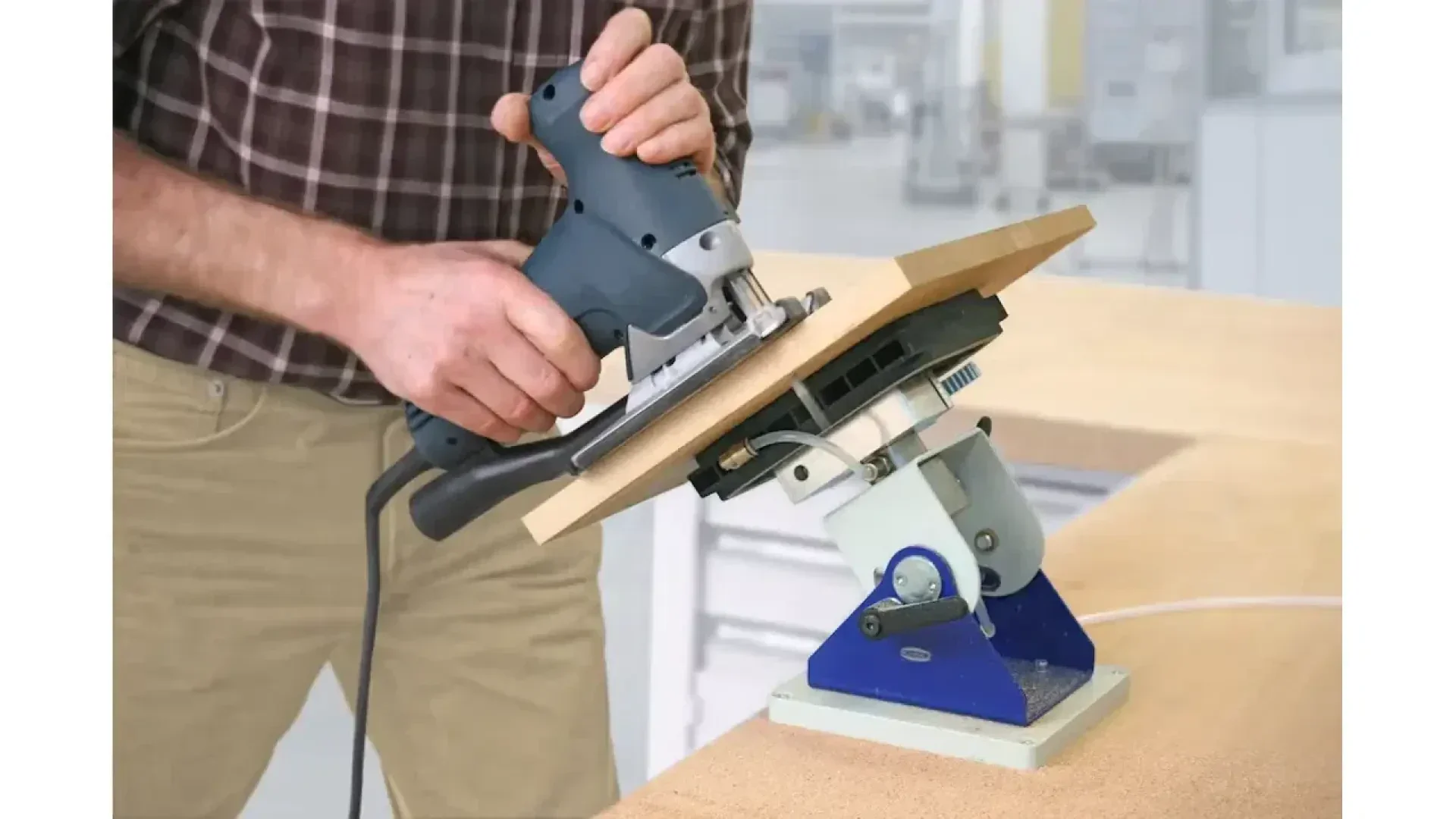 Une personne utilise une scie électrique manuelle pour découper une planche de bois, qui est fixée sur un étau bleu réglable monté sur un établi dans un atelier.