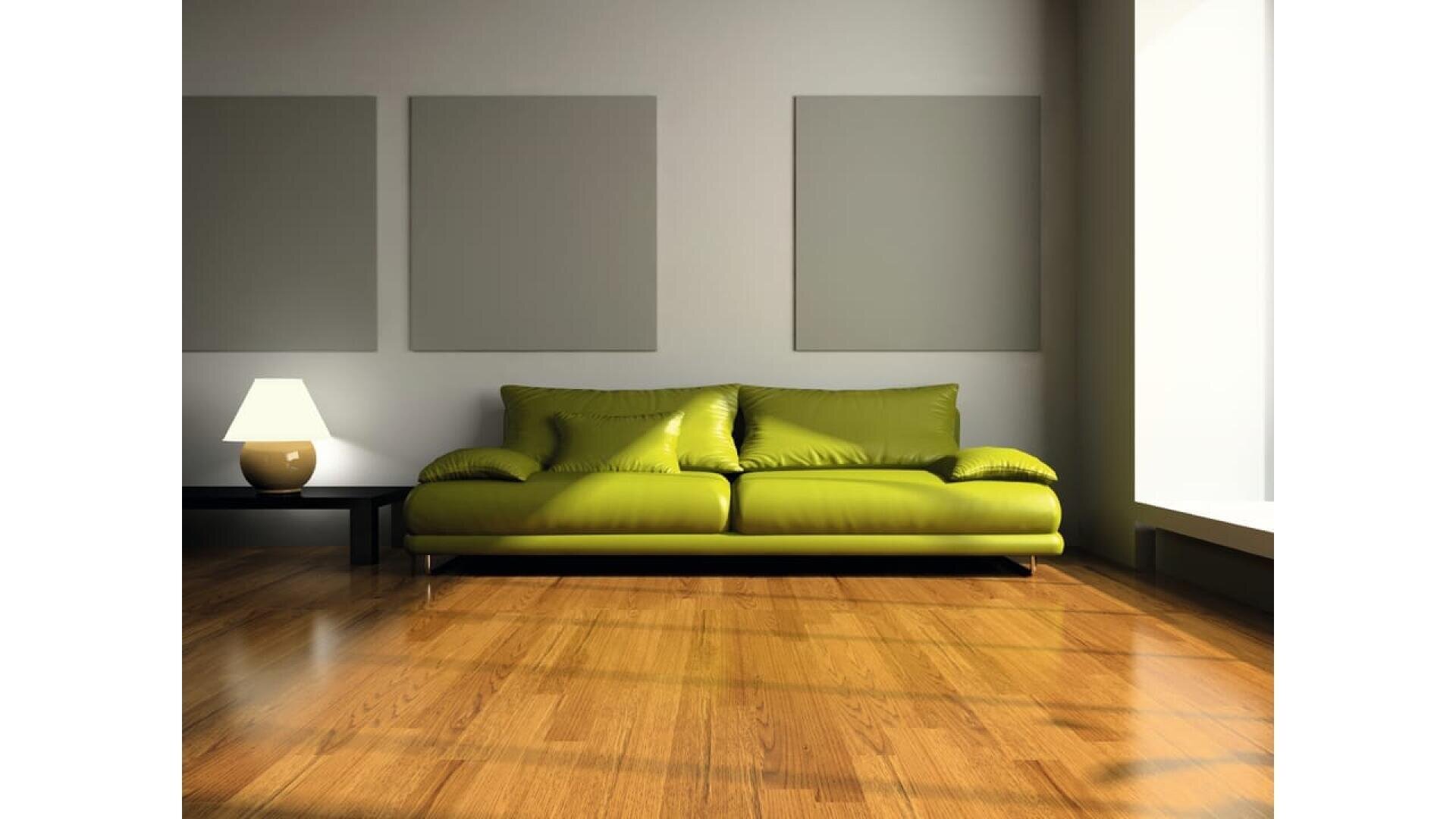 Un salon moderne avec un canapé vert, une petite table avec une lampe allumée, un sol en bois, trois panneaux muraux carrés et la lumière du soleil qui pénètre par une grande fenêtre sur la droite.