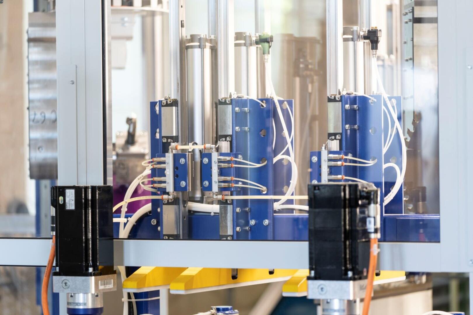 Nahaufnahme einer modernen automatisierten Industriemaschine mit blauen und silbernen Komponenten, Drähten und schwarzen Motoren in einer sauberen, gut beleuchteten Produktionsumgebung.