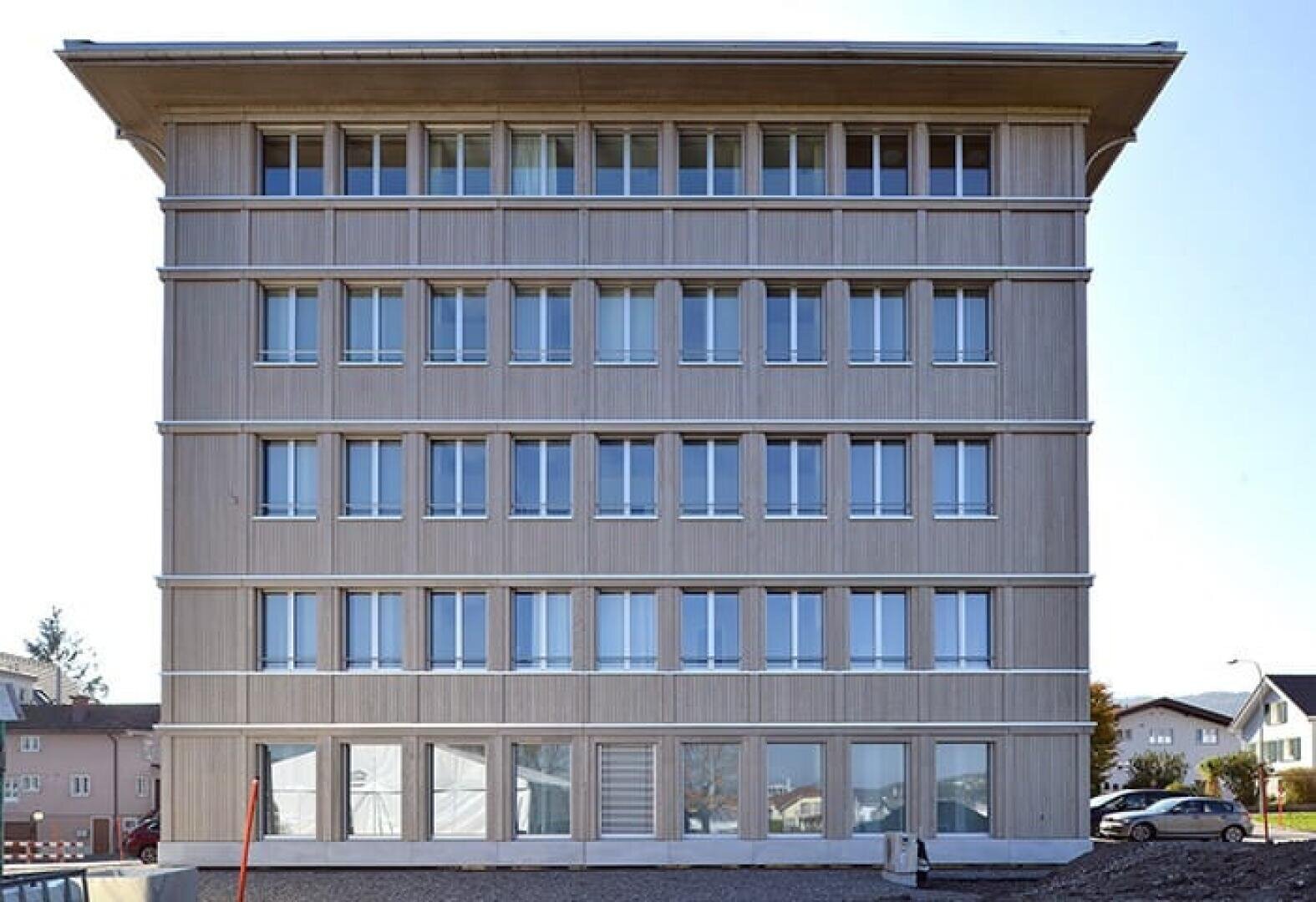 Ein modernes, fünfstöckiges Gebäude mit einer symmetrischen Fassade mit rechteckigen Fensterreihen und einer hellen Holzverkleidung in einem Wohngebiet mit klarem Himmel über dem Kopf.