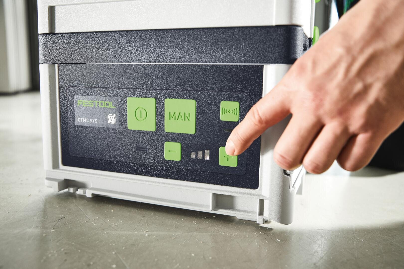 Eine Hand drückt eine grüne Taste auf dem Bedienfeld eines Festool-Geräts, das über mehrere Tasten und Anzeigen auf einer grau-schwarzen Oberfläche verfügt.