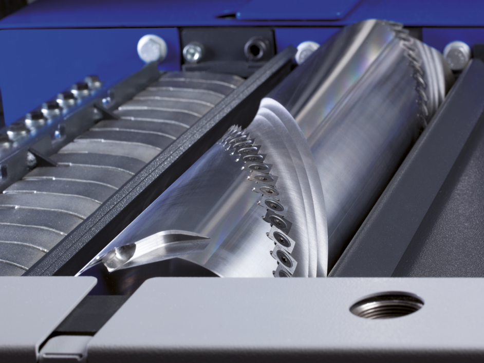Nahaufnahme eines glänzenden, zylindrischen Hobelmesserkopfs mit scharfen Klingen, der in einer Maschine positioniert ist, wobei metallische und blaue Komponenten sichtbar sind.