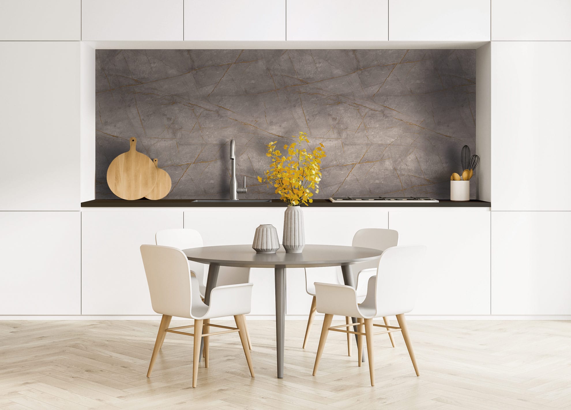 Cuisine moderne avec des armoires blanches, un dosseret en marbre gris et une table ronde avec quatre chaises blanches. Un vase avec des fleurs jaunes est posé sur la table ; des planches à découper et des ustensiles de cuisine sont posés sur le comptoir.