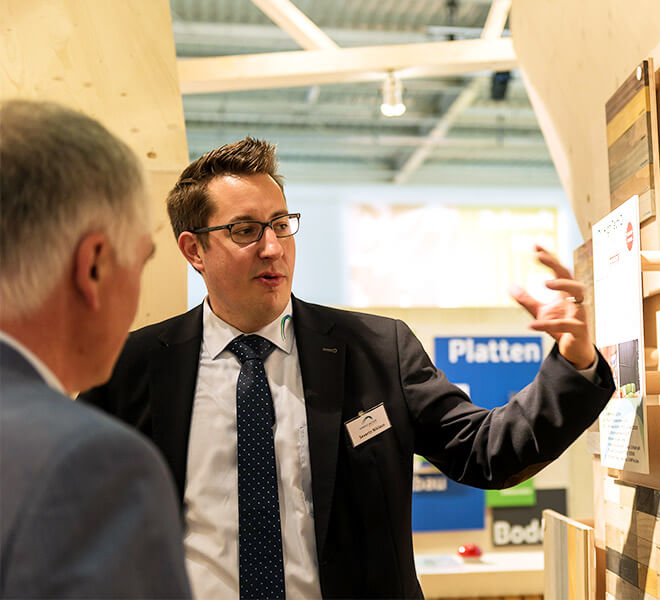 Un exposant du salon HOLZ explique à un client les détails de ses produits.