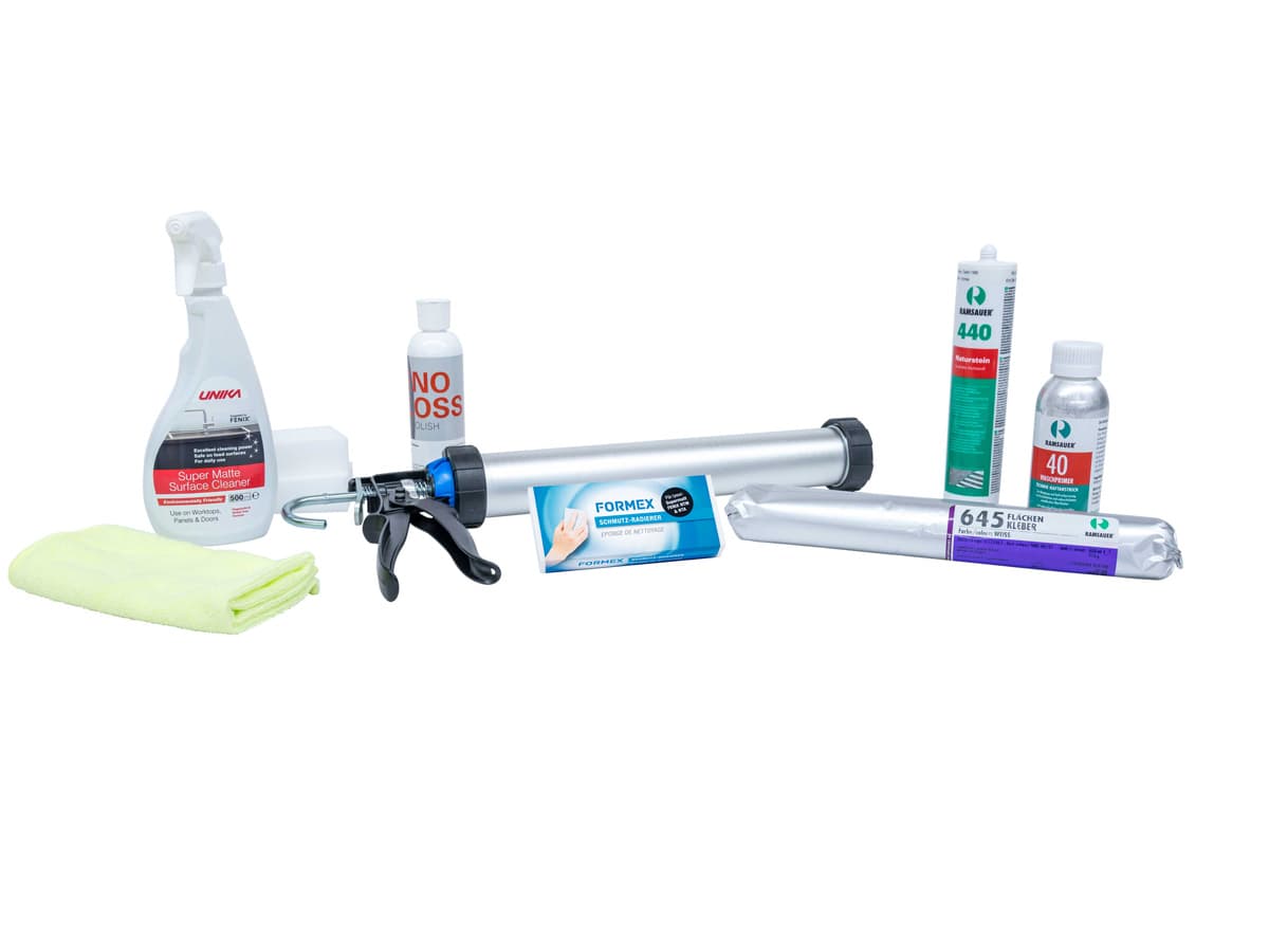 Sélection de produits de nettoyage et d'étanchéité, notamment un flacon pulvérisateur, un nettoyant pour les mains, un pistolet à calfeutrer, des tubes de mastic en silicone, un flacon de nettoyant, des lingettes nettoyantes et un chiffon jaune, le tout disposé sur un fond blanc.