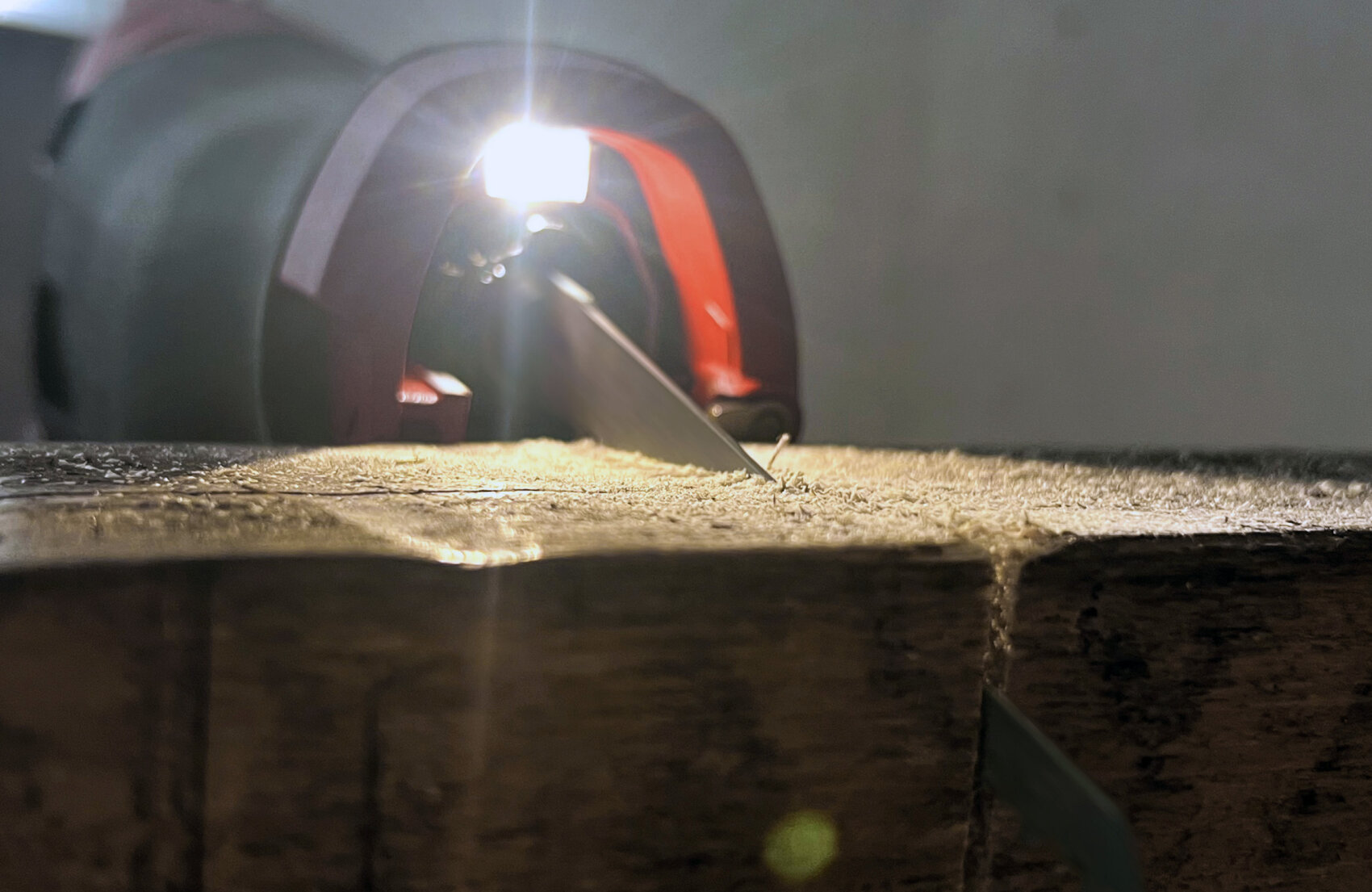 Nahaufnahme einer Motorsäge, die ein Holzstück durchschneidet, wobei Sägespäne sichtbar sind und ein helles Licht den Schnittbereich beleuchtet.